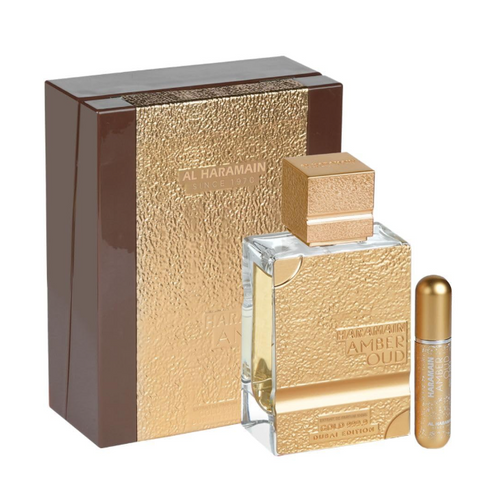 Al Haramain Amber Oud Eau de Parfum set, featuring a textured gold and brown outer box, a clear glass bottle with amber liquid and a gold cap, and a small matching gold roll-on bottle, all on a white background.