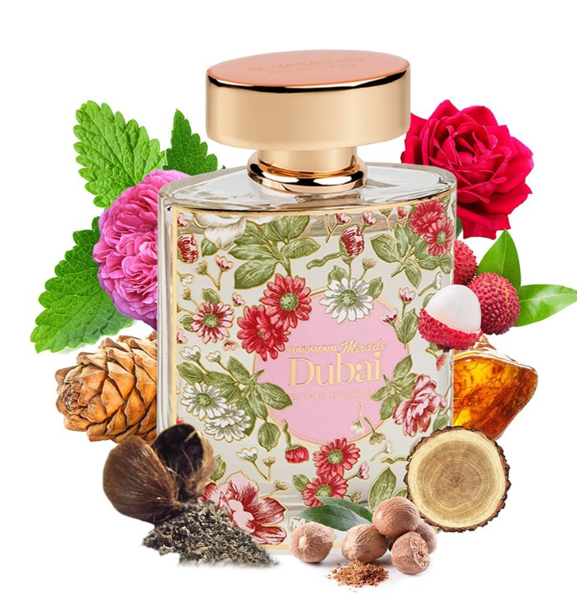 A perfume bottle labeled 'Al Haramain Miracle Dubai' surrounded by botanical and fruit ingredients including red roses, pink flowers, green leaves, lychee, pinecone, dried herbs, and nuts on a white background.