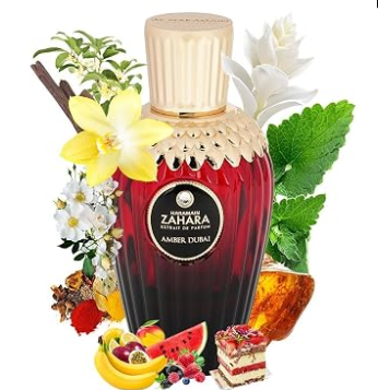 A bottle of Zahara Amber Dubai perfume with a gold cap and dark amber-red liquid, surrounded by decorative flowers, leaves, and fruit slices on a white background.