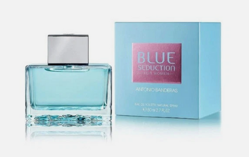 Blue Seduction For Women Eau de Toilette by Antonio Banderas, featuring a light blue glass bottle with a silver cap next to its light blue packaging box with a pink label.