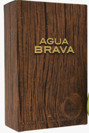 A rectangular wooden box for AGUA BRAVA cologne by PUIG, featuring a dark brown wood grain texture with gold lettering and a small green object partially visible at the right edge.