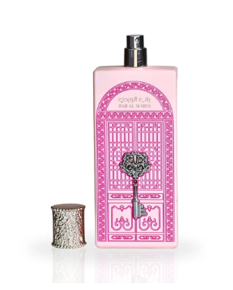 A pink rectangular perfume bottle with a silver spray top and a decorative pink door illustration on the front, shown next to a small silver cylindrical container on a white background.