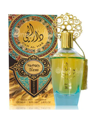 A perfume bottle with a gold cap and ornate gold hanging tassel, shown in front of its decorative illustrated box. The bottle contains yellow-green liquid with a blue base, and the box features gold, teal, and black ornamental artwork with Arabic text.