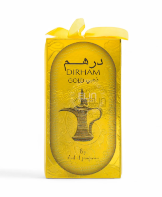 A yellow rectangular box with a matching yellow ribbon bow on top, featuring a gold Arabic calligraphy logo that reads 'Dirham Gold' and an illustration of a traditional Arabic teapot. The brand 'By Art of saffron' is printed at the bottom.