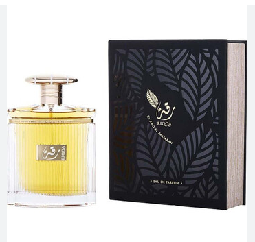 A bottle of Qasr Al Huda Eau de Parfum with golden-yellow liquid next to its black packaging box with silver leaf patterns.