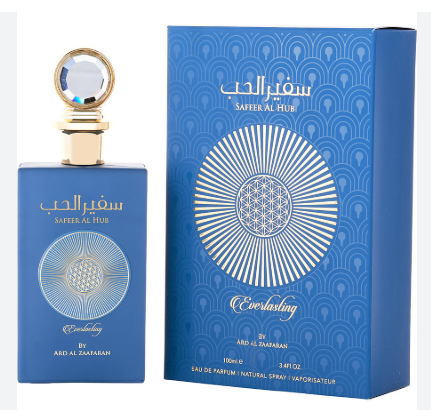 A blue perfume bottle with a gold cap stands beside its matching blue box. The bottle and packaging feature white Arabic script, the English name 'SAFFER AL FADH', a circular geometric floral design, and the word 'Everlasting'.