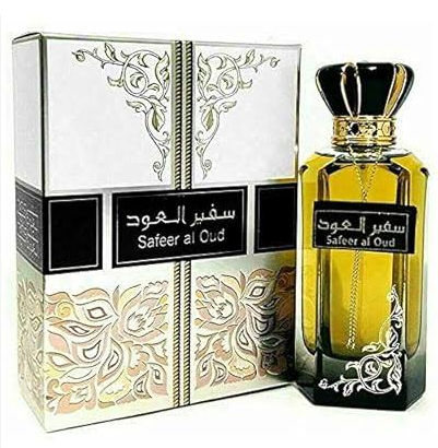 Safeer al Oud perfume bottle and its ornate packaging box. The bottle is made of transparent amber glass with a black cap and gold detailing, and the box features white and gold floral patterns with black bands.