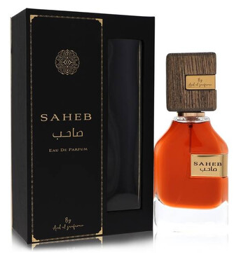 A bottle of Saheb Eau de Parfum with amber liquid and a dark wood cap, shown next to its black presentation box with gold lettering.