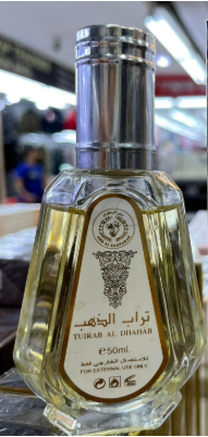 A 50ml bottle of Turab Al Dhahab tea oil, featuring a clear glass bottle with a silver cap and a gold label with Arabic and English text.