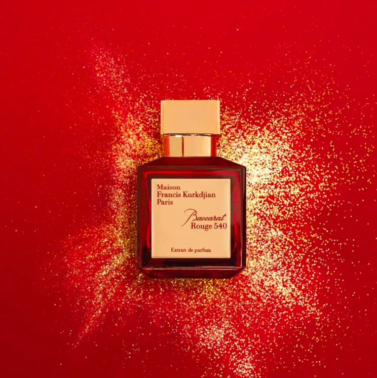 A bottle of Maison Francis Kurkdjian Paris 'Paisonnier Rouge 540' perfume, featuring a dark red glass bottle with a gold cap and a cream-colored label, set against a vibrant red background with gold glitter.