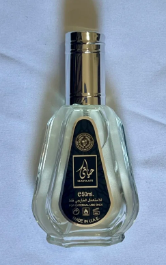 A 50ml clear glass bottle of Sargamhani perfume with a shiny silver cap and a black label featuring gold and white details, set against a light blue fabric background.