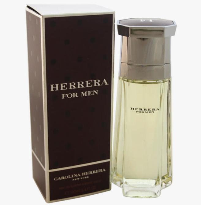 Herrera For Men cologne bottle with a faceted clear glass body showing pale yellow liquid, standing next to its dark brown box with silver lettering.