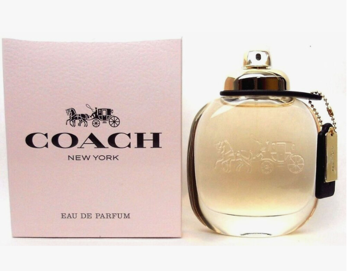 Coach New York Eau de Parfum bottle next to its signature pink box, featuring a gold-tone cap and a leather tag with a horse-drawn carriage emblem.