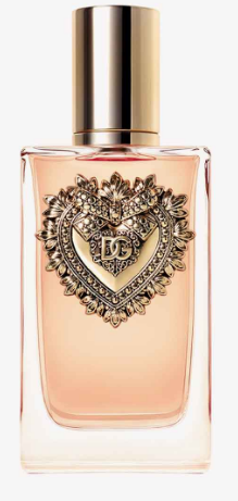 A bottle of Dolce & Gabbana perfume with a metallic gold cap and a large ornate heart-shaped gold emblem on the front, containing a pale peach-colored liquid, set against a plain white background.