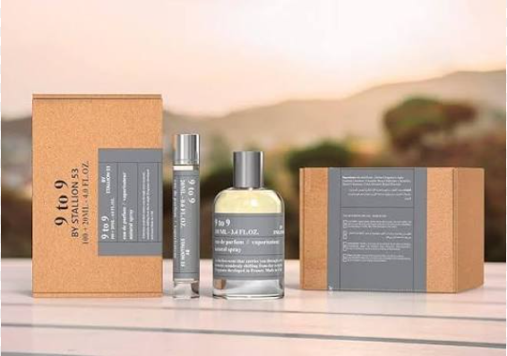 A perfume bottle and matching travel spray with two brown kraft paper boxes, displayed on a light surface against a blurred outdoor background. The product label reads '9 to 9 BY STALLION 53' and 'Fior de Parfum'.