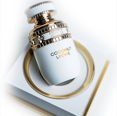 A luxury perfume bottle labeled 'COCONUT LECHE' by Fretissure Avignon, featuring a white body with gold metallic accents and a textured gold cap, resting on a white geometric pedestal with a gold ring.
