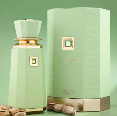 A pale mint green perfume bottle with gold trim stands beside its matching textured box. The bottle and box both feature a small square green gem detail and the brand name is faintly visible near the bottom.