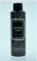 A black aerosol can of GUESS UOMO Est. 1981 deodorizing body spray, featuring a black and white marble pattern with a silver geometric border label, set against a light blue background.