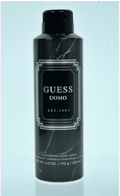 A black aerosol can of GUESS UOMO Est. 1981 deodorizing body spray, featuring a black and white marble pattern with a silver geometric border label, set against a light blue background.