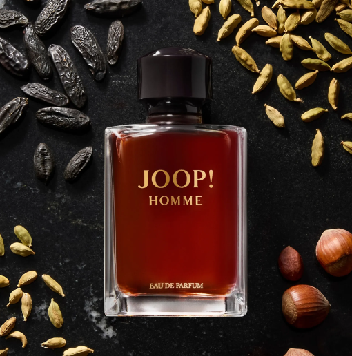A bottle of Joop! Homme Eau de Parfum with amber-brown liquid and gold lettering, styled on a dark textured background with spices and nuts.