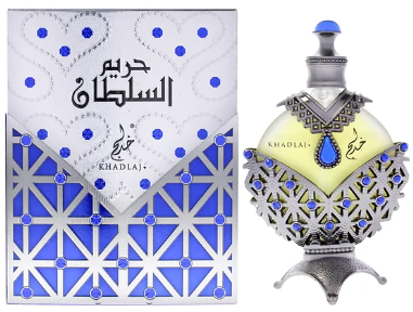 Khadraj perfume bottle and its matching box. The bottle is ornate with a silver filigree body, a pale yellow heart-shaped center, and a blue teardrop gem.