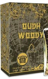 A boxed fragrance product labeled 'Oud Woody' with ornate gold decorative artwork on a dark olive-green box. A small perfume bottle is partially visible at the right edge.