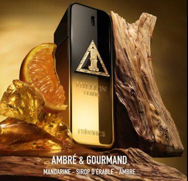 A bottle of Ambre & Gourmand fragrance by Rebeille, styled with amber liquid, orange slices, ice, and wood on a warm brown background. The bottle is black with a gold triangular logo and gold lettering.