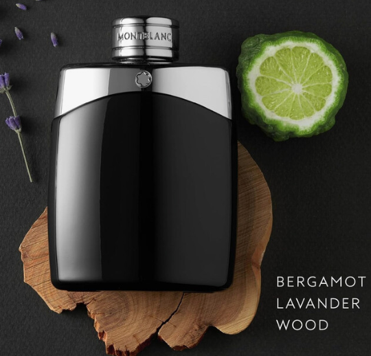 A glossy black perfume bottle with a silver cap engraved 'MONTCLANC' is arranged on a wood slice over a dark background, with a sliced lime and lavender sprigs as props. White text reads 'BERGAMOT LAVANDER WOOD'.