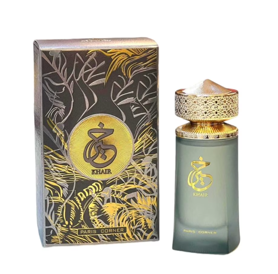 A bottle of Khair Paris Corner fragrance next to its decorative packaging box. The bottle is frosted gray-green with a textured gold cap and gold logo, while the box features a black and gold botanical pattern with a gold circular logo.