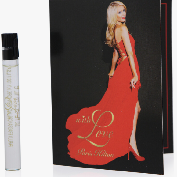 A perfume sample vial with a black cap and clear liquid stands next to a black card featuring a blonde woman in a red gown and the text 'with Love Paris Hilton'.