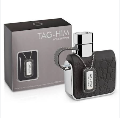 TAG-HIM Pour Homme fragrance bottle with a textured black body and silver cap, shown next to its gray retail box on a white background.