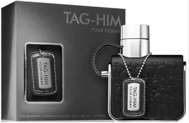 TAG-HIM Pour Homme fragrance shown with its black retail box and a black textured perfume bottle featuring a silver cap and a dog-tag style label.