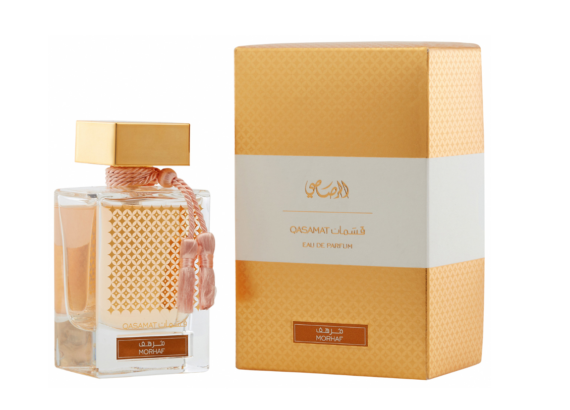 A perfume bottle with a gold cap and pink tassel next to its matching gold and white packaging box, labeled 'Omanat Al-Aqsa' and 'Honesay'.