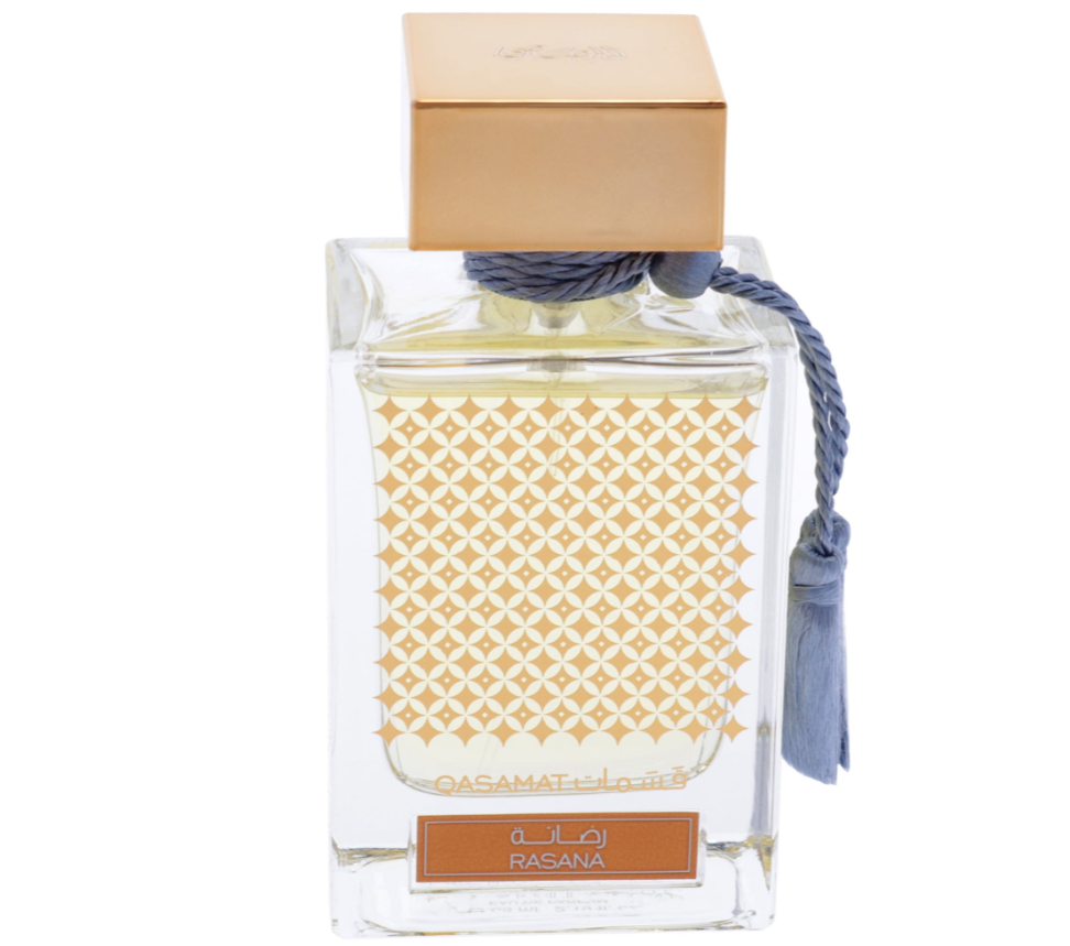 A clear glass perfume bottle with a gold geometric patterned insert, a gold cap, and a blue tassel cord, labeled Rasana by Qasamat for Her.