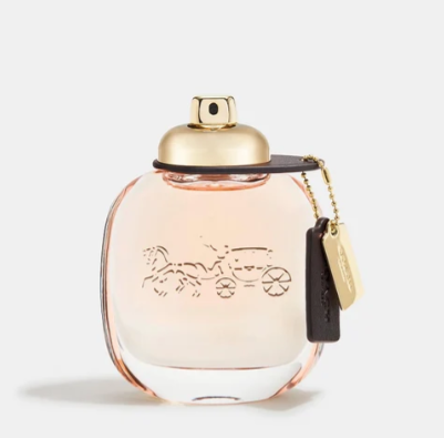 A Coach perfume bottle with a gold cap and a hanging black leather keychain tag featuring the Coach logo, set against a clean white background.
