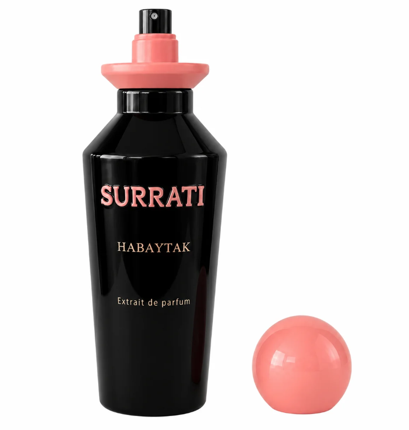 A black cylindrical perfume bottle labeled 'Surrati Habaytak Extrait de parfum' with a coral pink spray top, shown alongside a matching coral pink spherical object on a plain white background.