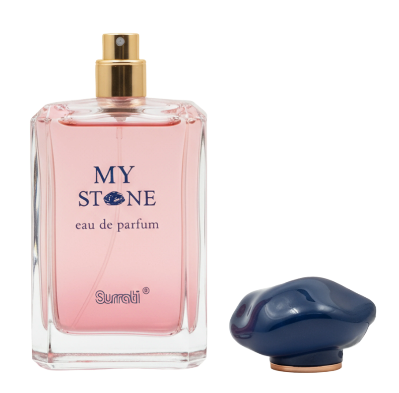 A clear rectangular perfume bottle filled with pink liquid, labeled 'MY STONE eau de parfum' and 'Surrati', shown on a white background with a dark blue cap placed beside it.