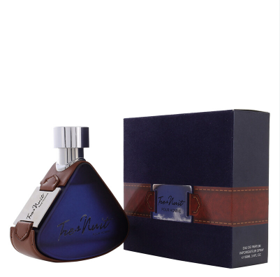 A bottle of Theo Nait Cologne with a dark blue triangular body and brown leather-like trim, shown next to its matching dark blue box with a brown band and silver logo plaque.