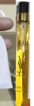 A close-up of a YSL Saint Laurent perfume spray vial with a gold cap, held next to a white cloth.