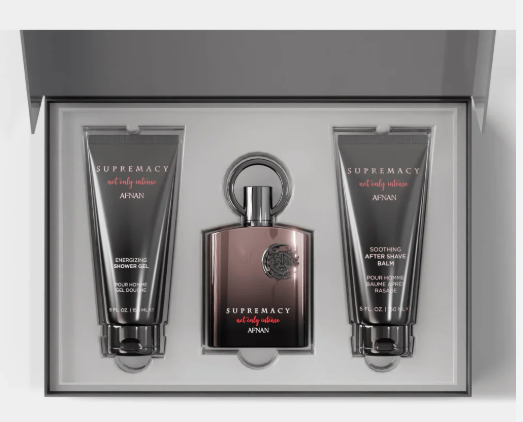 A boxed fragrance gift set from AFNAN, featuring a central bottle of 'Supremacy' cologne with a metallic rose-gold cap and base, flanked by two dark gray tubes of shower gel and body wash in a light gray presentation box.
