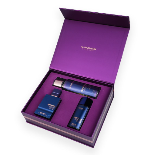 An open luxury gift box in deep purple with three blue fragrance and grooming products inside, branded Al Haramain. The set includes a cologne bottle, a body spray canister, and a smaller bottle, arranged in a custom purple insert.