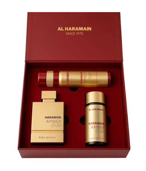 Al Haramain Amber Oud Ruby Edition fragrance gift set in a red box, containing a gold perfume bottle, a gold body spray can, and a gold cylindrical bottle.
