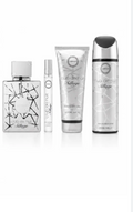 Four Milly Beauty cosmetic and fragrance products arranged on a white background: a square perfume bottle with a black geometric pattern, a small travel spray, a silver tube labeled body butter, and a tall silver bottle labeled hair oil.