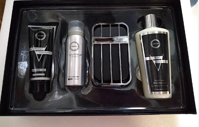 A men's grooming gift set in a black tray, containing a black and silver shower gel tube, a silver deodorant canister, a black and silver hair dryer cover, and a silver and black shampoo bottle.