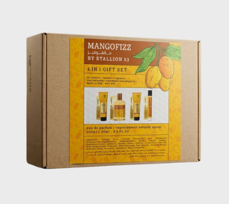 A boxed fragrance gift set labeled 'MANGOFIZZ BY STALLION 53' in Arabic, shown on a plain light gray background. The package is brown cardboard with a large yellow-orange front panel featuring mango illustrations and small product photos of bottles and tubes.