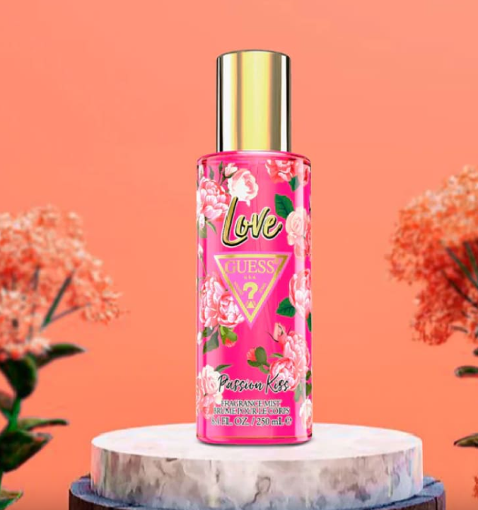 Guess Love Passion Kiss Deodorant Spray bottle on a marble pedestal against a peach background with decorative flowers.