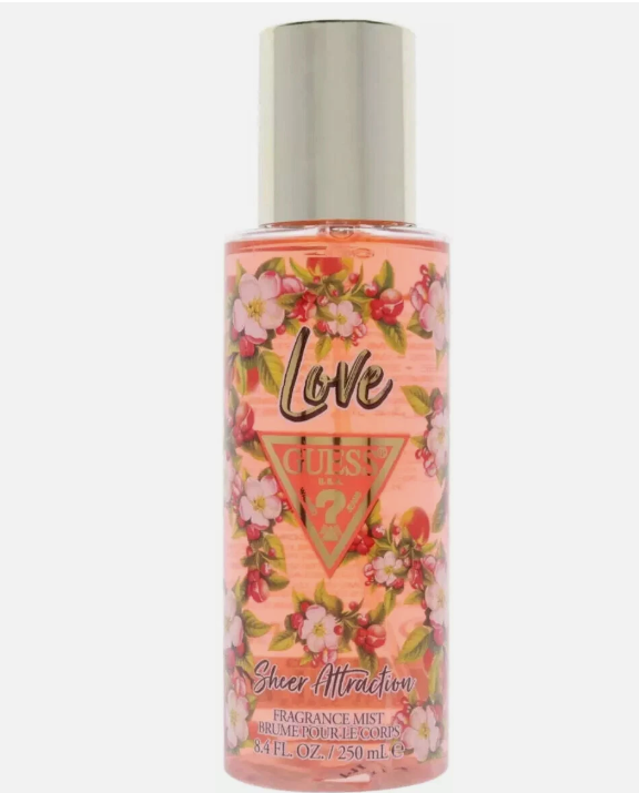 A bottle of Guess Love Sheer Attraction fragrance mist, featuring a pink floral label with cherry blossoms and a silver cap, on a light gray background.