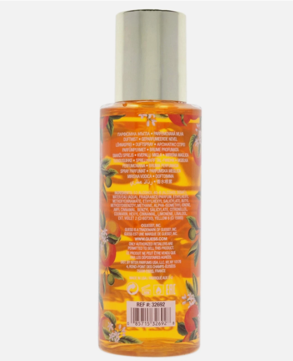 A bottle of body spray shown from the back, featuring a silver cap and a label with orange liquid, botanical illustrations, and dense text on a light gray background.