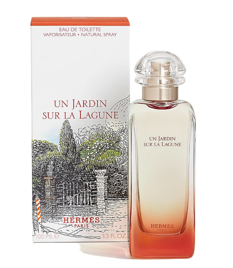 Hermes Un Jardin Sur La Laguna Eau de Toilette perfume bottle with a clear cap and orange gradient base, shown next to its white and orange packaging box featuring a black line drawing of a garden.