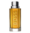 A bottle of Hugo Boss The Scent cologne with amber-yellow liquid inside a clear glass bottle, featuring a metallic silver cap and the brand name 'BOSS' printed vertically in gold on the front.